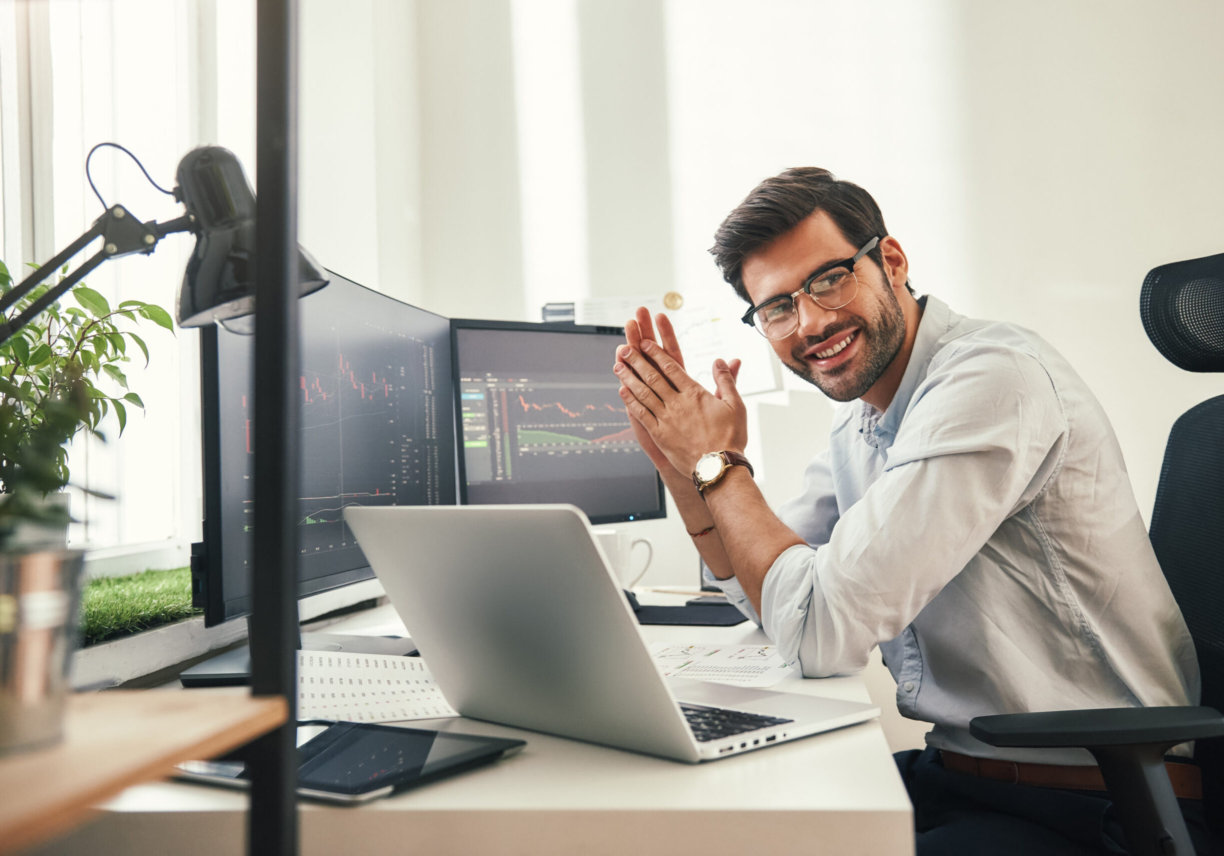 Young and successful. Happy bearded trader in formal wear and eyeglasses looking at camera and smiling while sitting in his modern office. Young and successful. Happy bearded trader in formal wear and eyeglasses looking at camera and smiling while sitting in his modern office. Stock broker. Forex market. Trade concept
