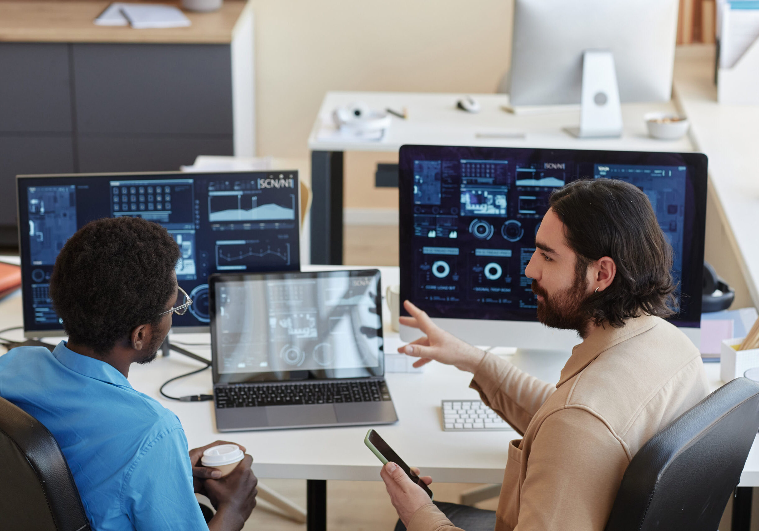 Young confident IT engineer explaining graphic data on computer screens to his colleague while looking at him during working meeting